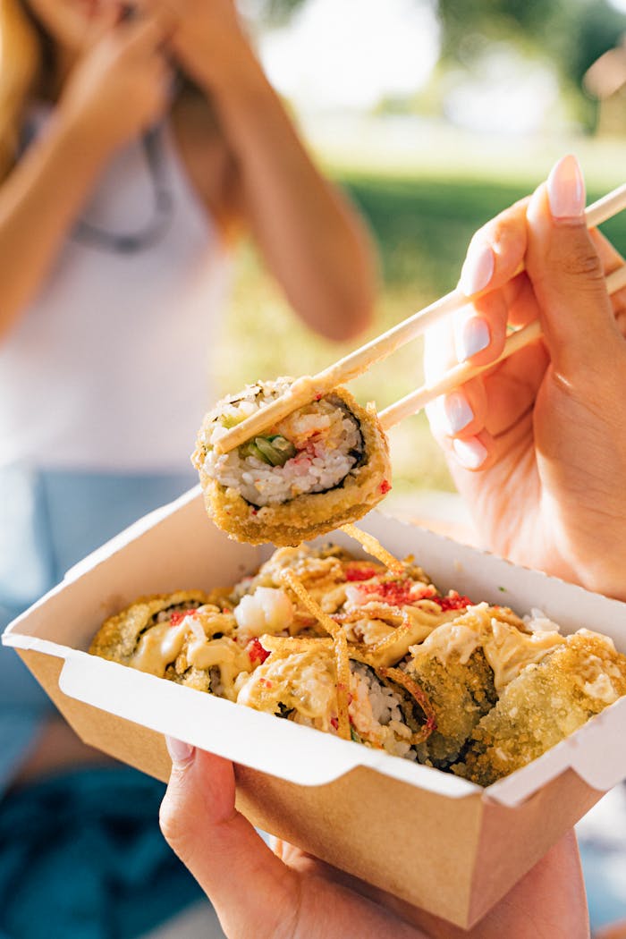 Close-up of sushi rolls held with chopsticks outdoors. Perfect for Asian cuisine lovers.