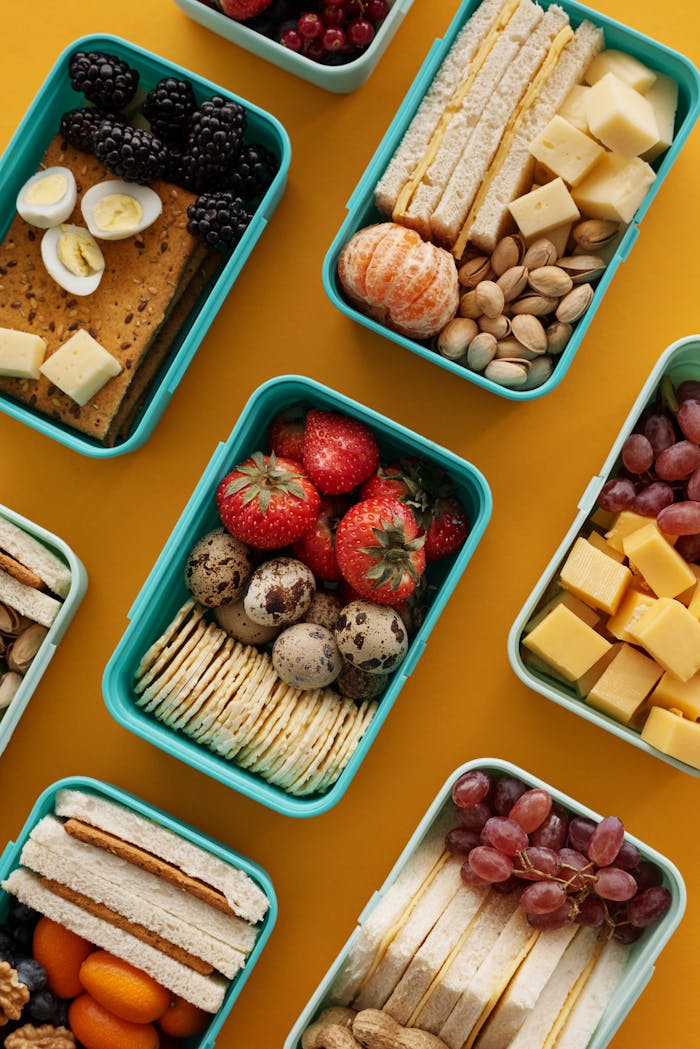 Top view of diverse snacks in bento boxes on yellow background.